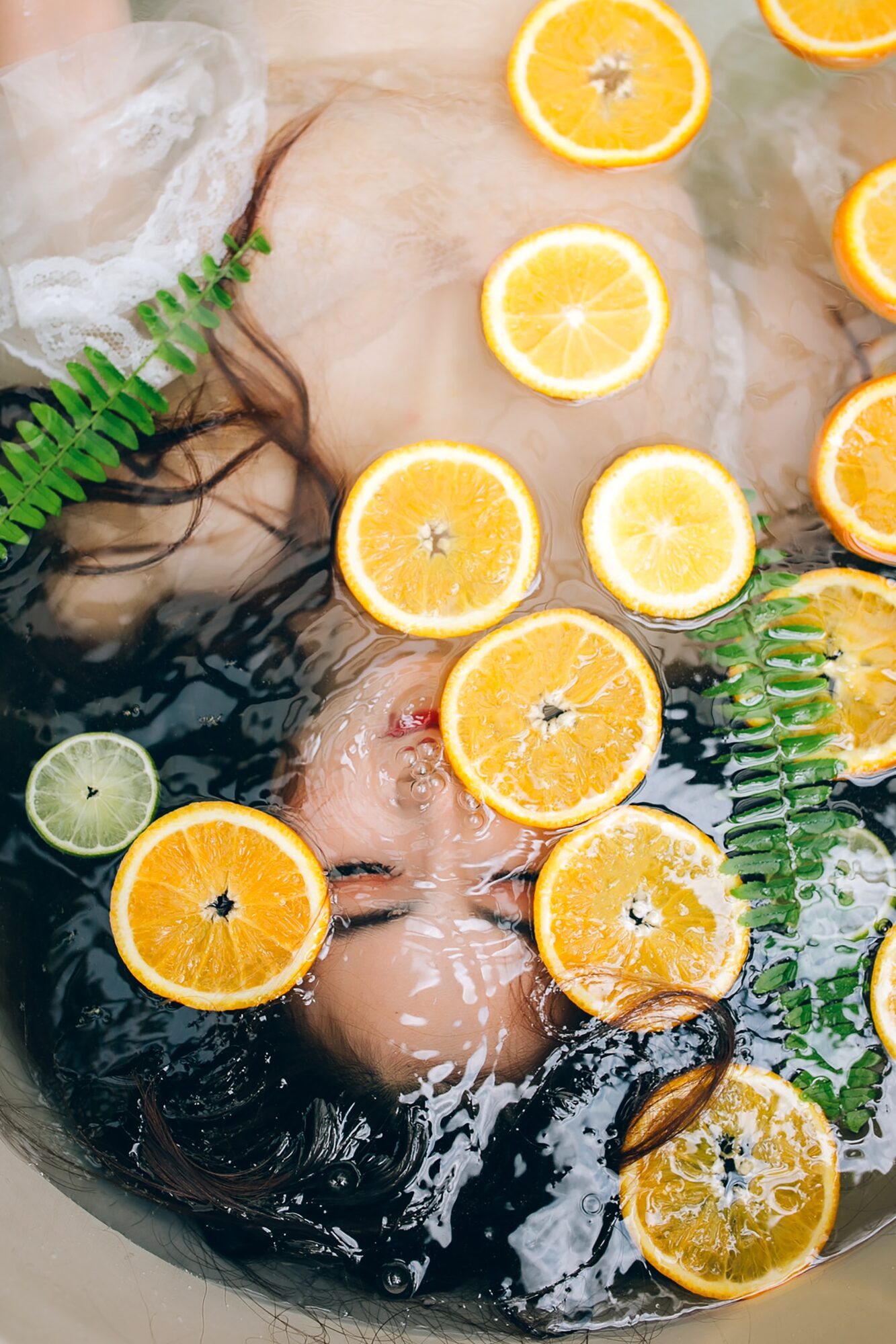 Bather among floating citrus and ferns, a natural-wellness ritual